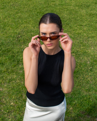 Julie wearing sleeveless Alicia Top with brown tinted animal pattern frame  cat-eye sunglasses with white satin silk skirt. 